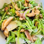 Wild Mushroom Salad with Shaved Manchego over Baby Arugula featuring tender sautéed mushrooms and thin slices of cheese.