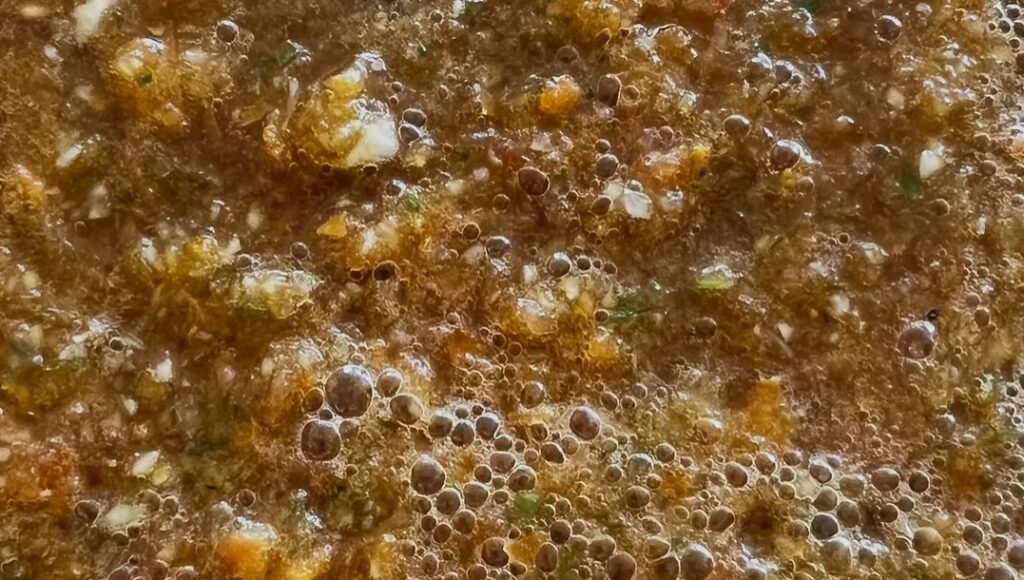 Rustic homemade gazpacho with finely blended vegetables, small herb pieces, and a lightly textured surface.
