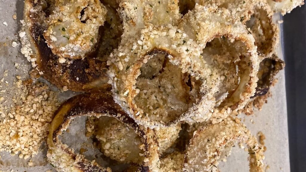 Crispy Gluten-Free Beer Battered Onion Rings with a golden, textured coating arranged on a baking sheet.