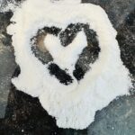 A heart drawn in white flour spread across a dark stone countertop.