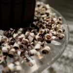 Homemade milk, dark, and white chocolate curls scattered across a clear glass plate.