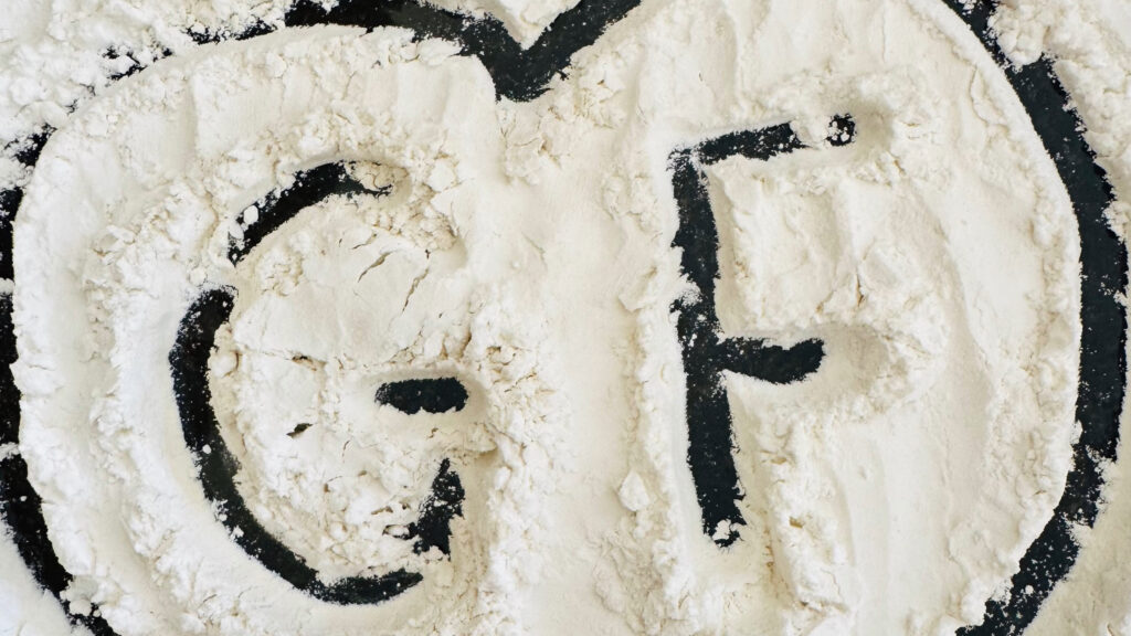 The letters GF written in white flour with a heart drawn around them on a dark surface.