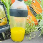 Shaker bottle filled with bright yellow lemony thyme dressing beside a lantern and fresh herbs in a garden.