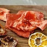 Crispy spicy oven-dried watermelon pieces served with dried citrus slices on a wooden board.