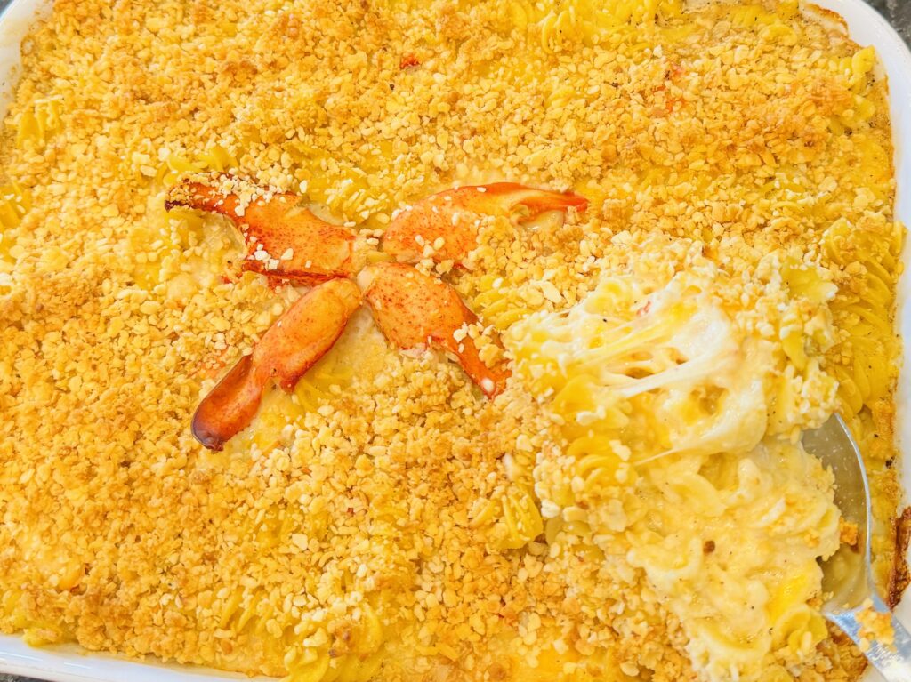 Gluten-free lobster mac and cheese with a golden breadcrumb topping and lobster claws in a white baking dish.
