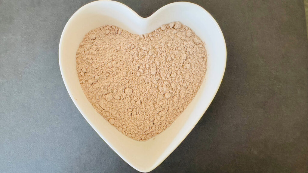 Light brown flour in a white heart-shaped bowl on a dark surface